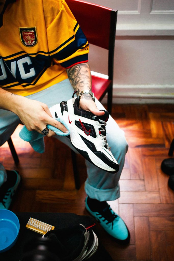 pexels-photo-4914582-4914582 A tattooed adult cleaning trendy sneakers indoors, focusing on footwear details.